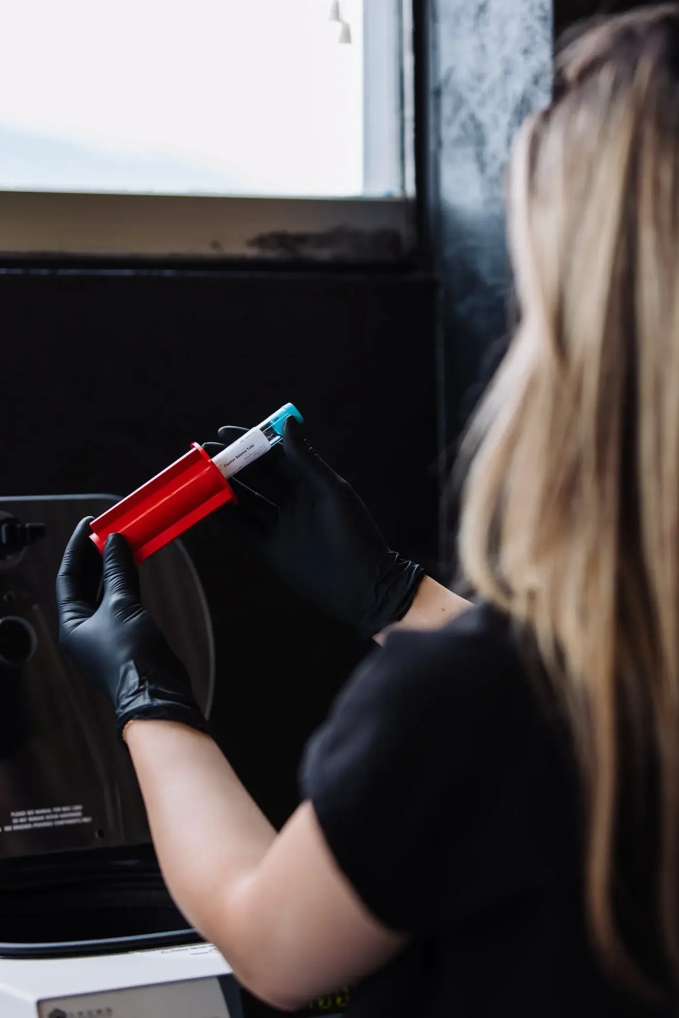 Gloved hands loading a tube into a red centrifuge bucket